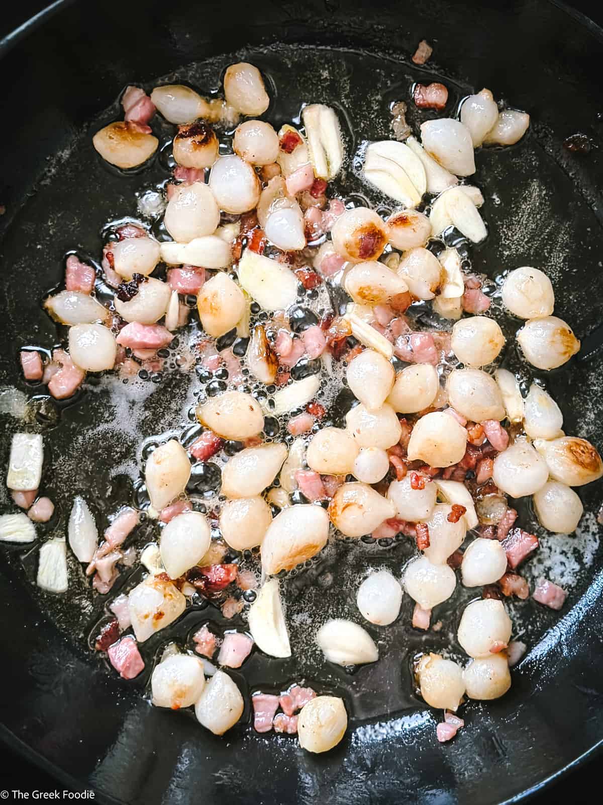 Pearl onions, diced bacon and garlic cooking in a skillet.
