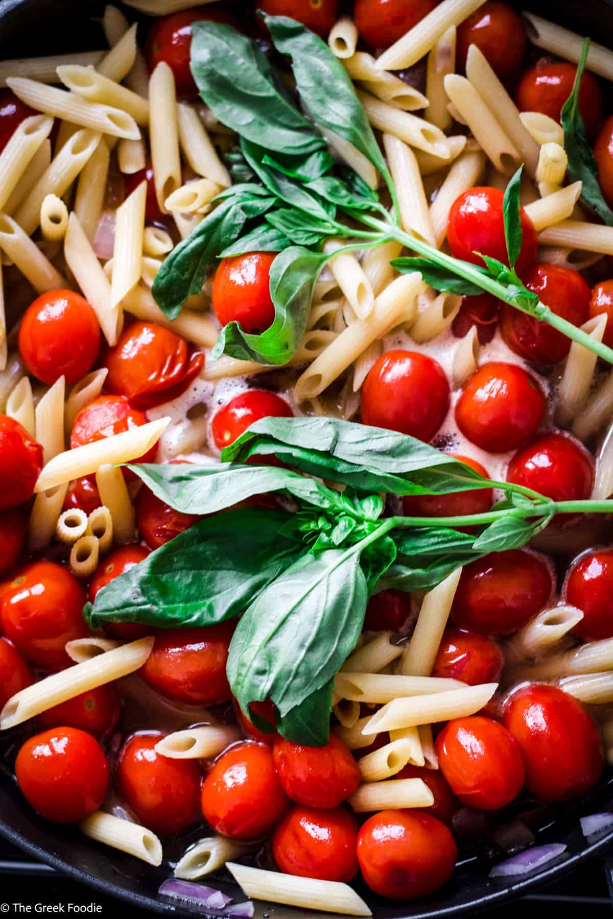 Pasta, fresh basil and cherry tomatoes in a deep skillet.