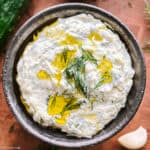 A bowl with tzatziki with chopped dill on top.