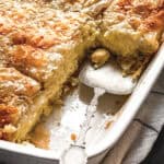 A pan with baked Greek cheese pie with some pieces cut and a serving utensil.