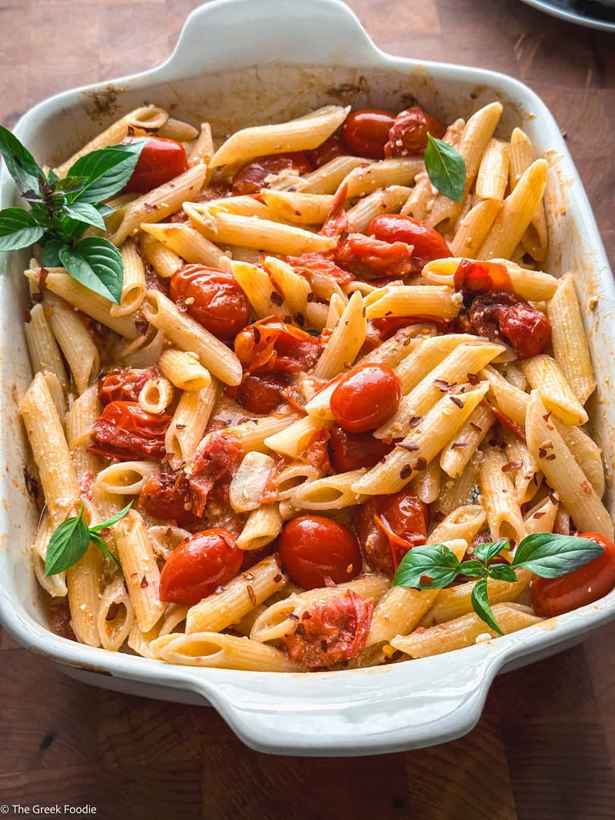 A baking pan with pasta with tomatoes and feta and fresh basil.