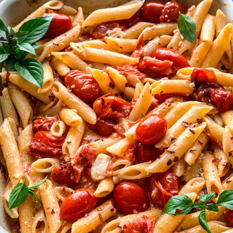 A baking pan with pasta with tomatoes and feta and fresh basil.
