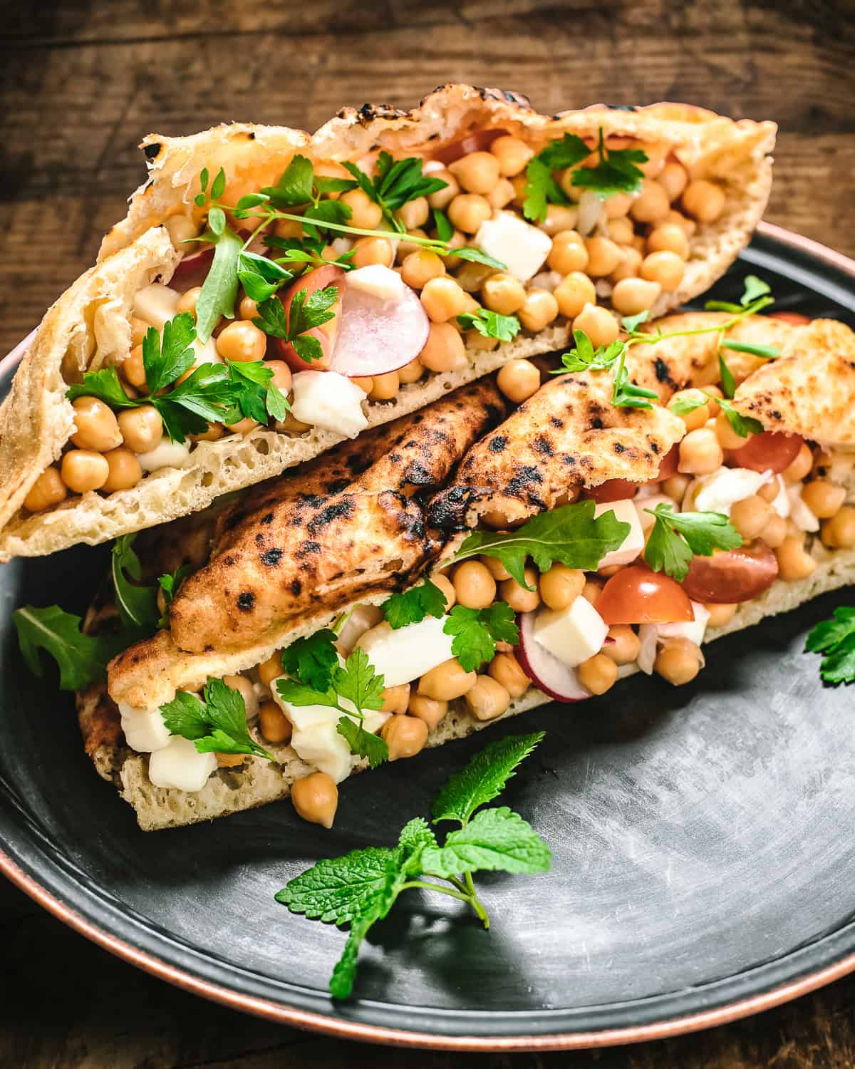 Two pitas filled with veggies, hummus and chickpeas on a plate.