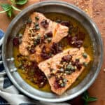 Two salmon fillets in a skillet with brown butter sauce, on a table.