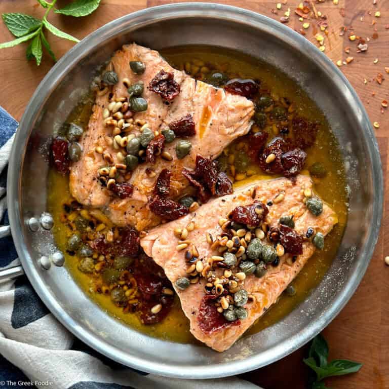 Two salmon fillets in a skillet with brown butter sauce, on a table.