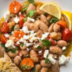 A plate with Greek braised beans with tomatoes and carrots and lemon halves.