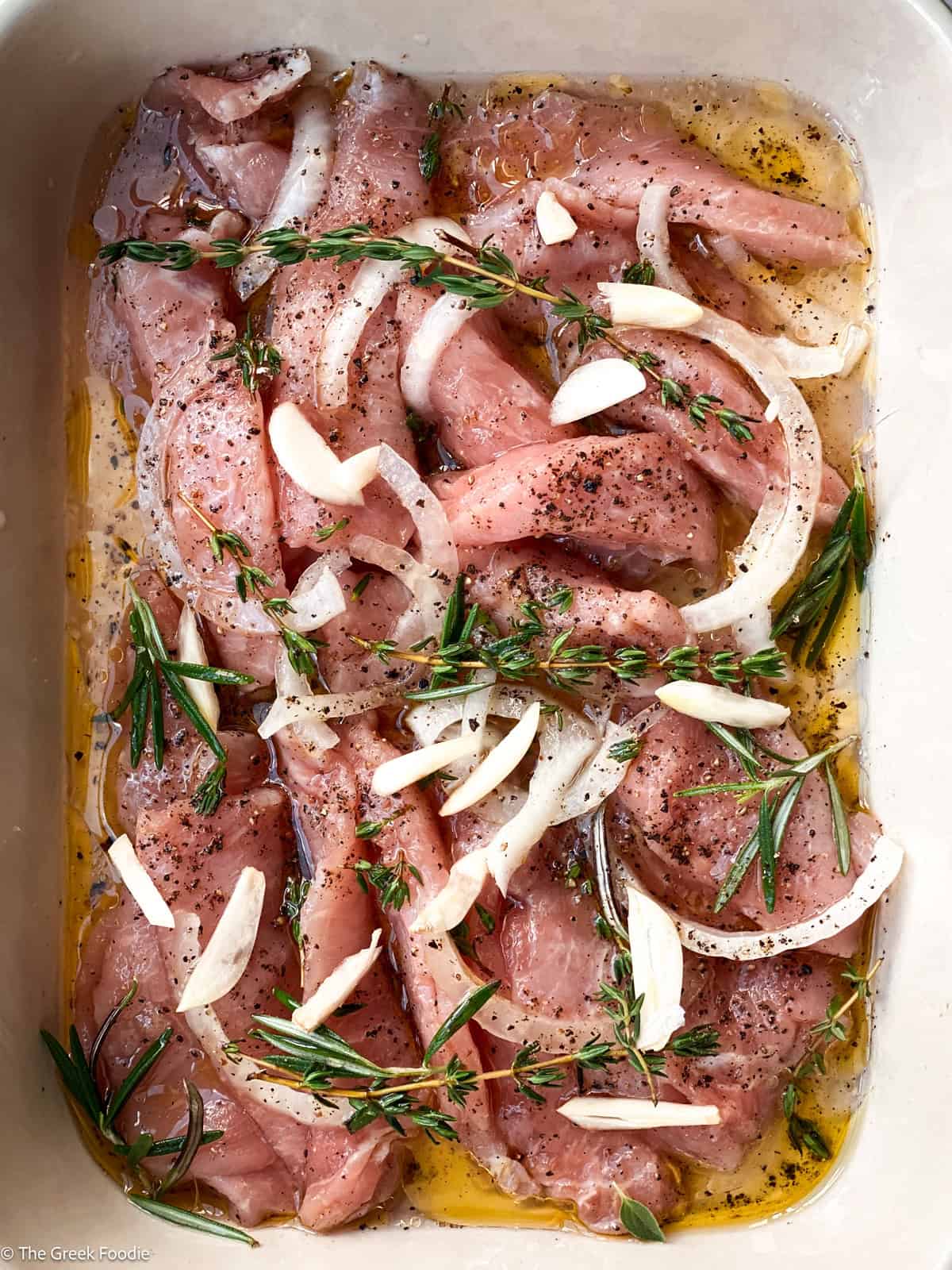 Pork marinating in olive oil with fresh herbs, onions and garlic.