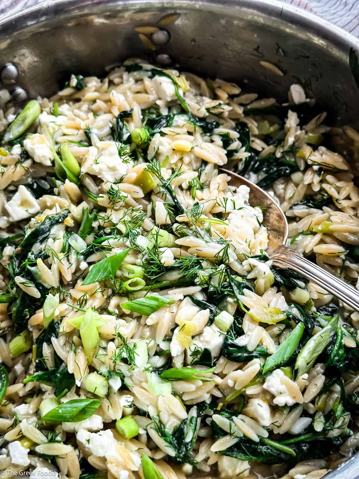 Close up of orzo with spinach and feta with a spoon.