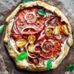 A tomato galette with feta cheese, onions and tomatoes on a cutting board.