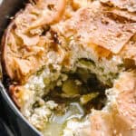 A baking pan with boureki with one piece of pie out.