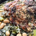 A roasted pork and beans in a dark roasting pan.