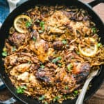 A cast iron skillet with lemon orzo chicken and two serving utensils on a table.