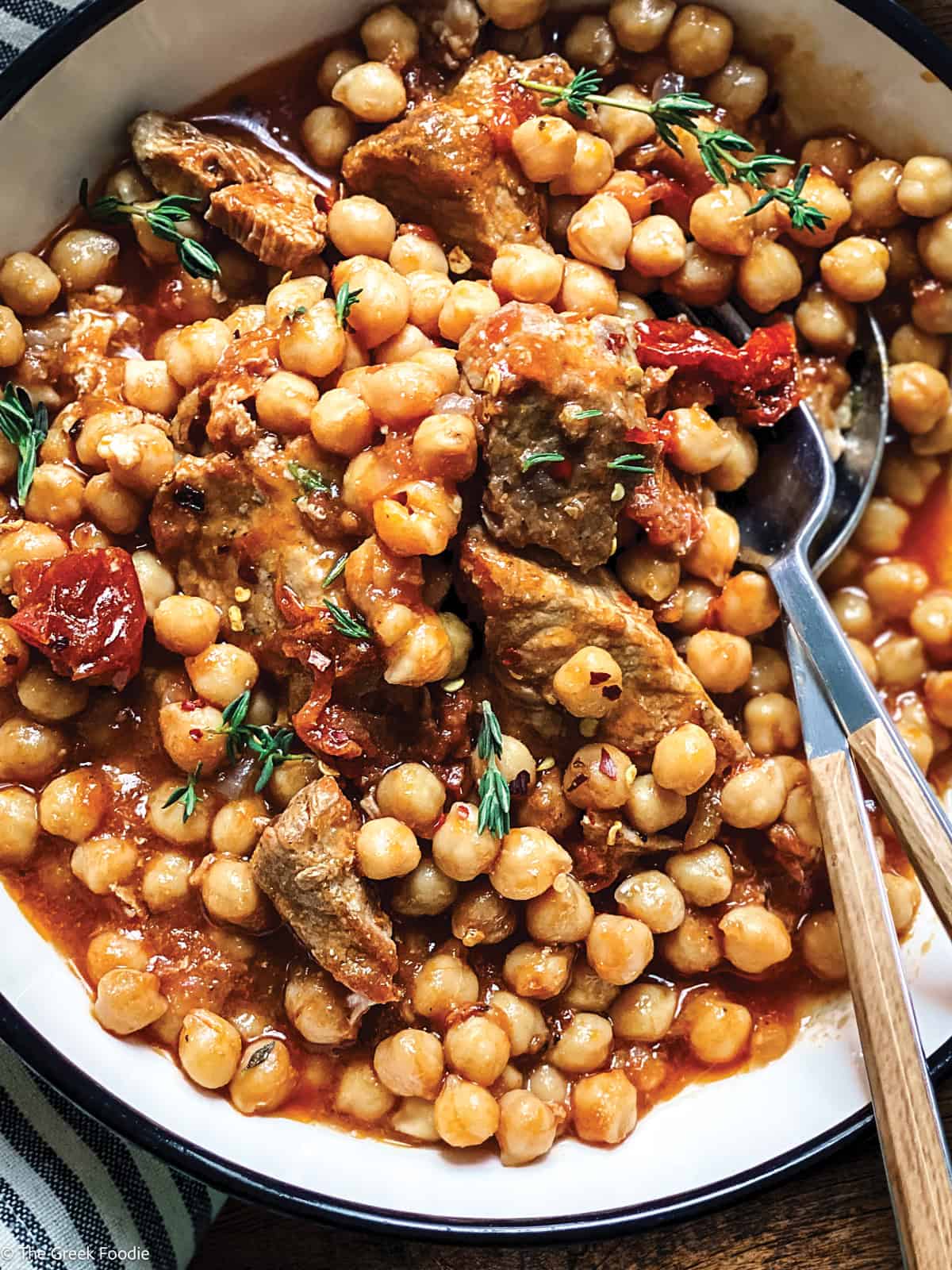 Pork Stew With Chickpeas in a plate with a fork and spoon, over a cloth napkin.