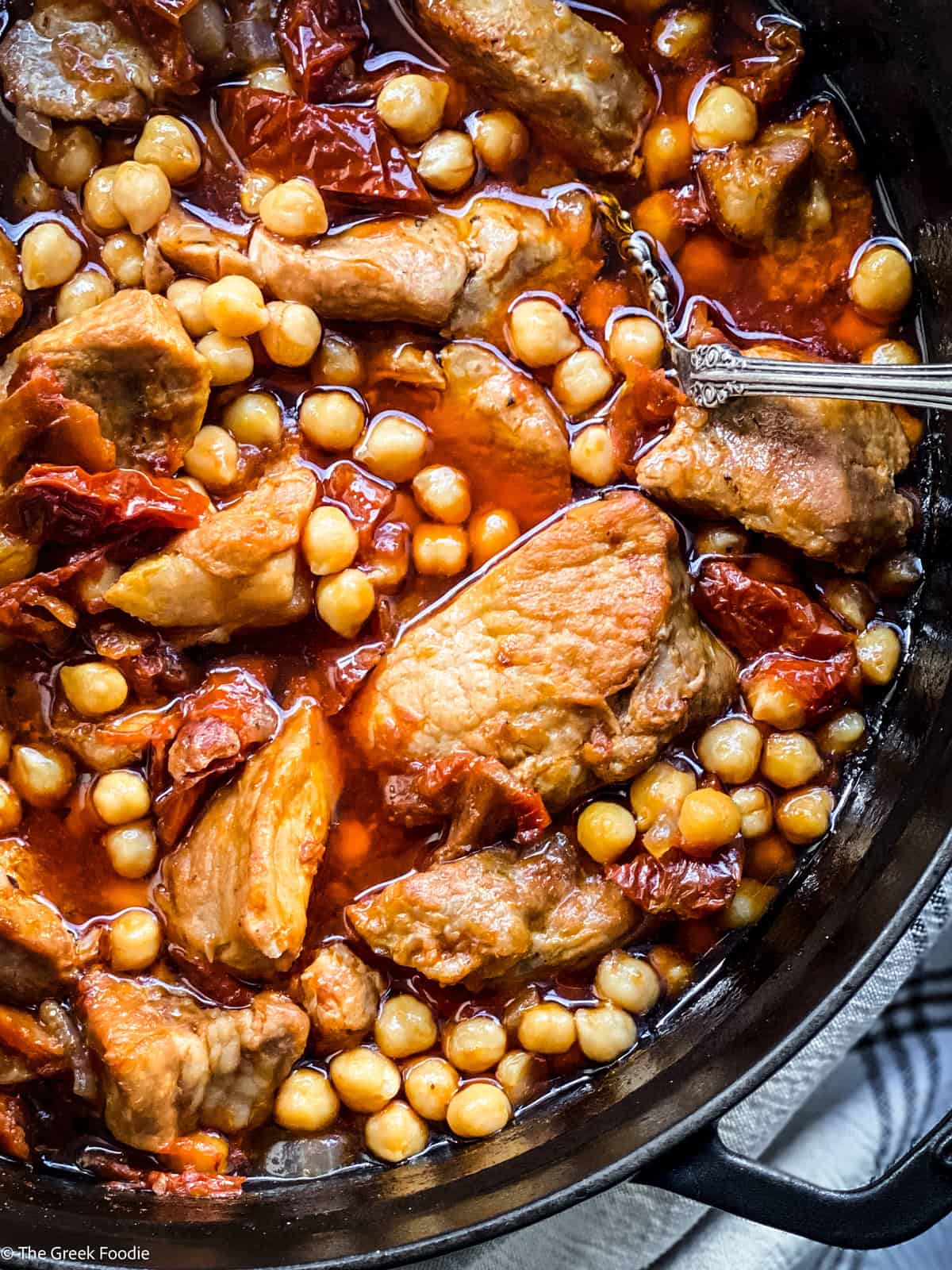 Greek pork stew with chickpeas in a Dutch oven with a silver spoon.