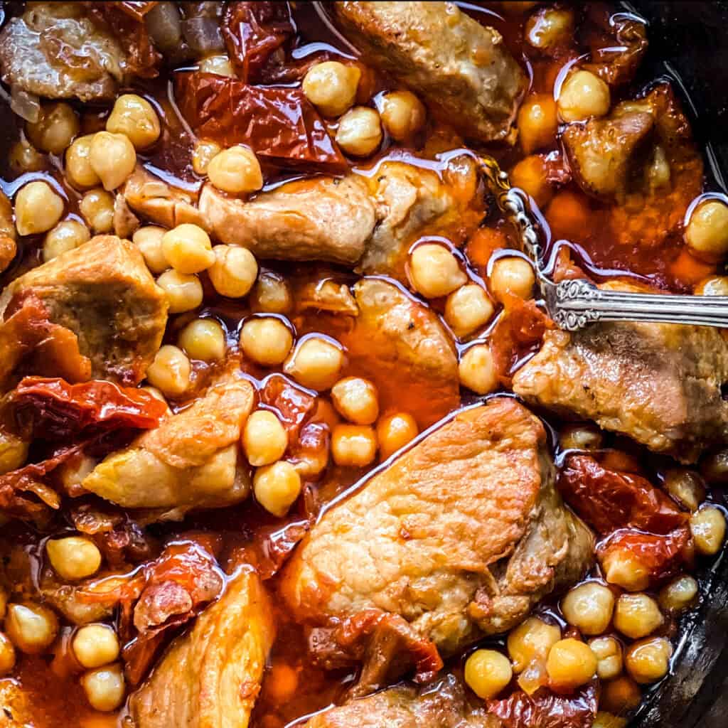 Pork Stew With Chickpeas in a dutch oven with a silver serving spoon.