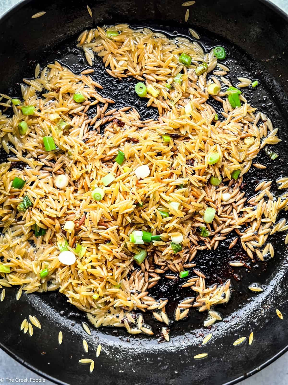 Toasting orzo and spring onions in a skillet.