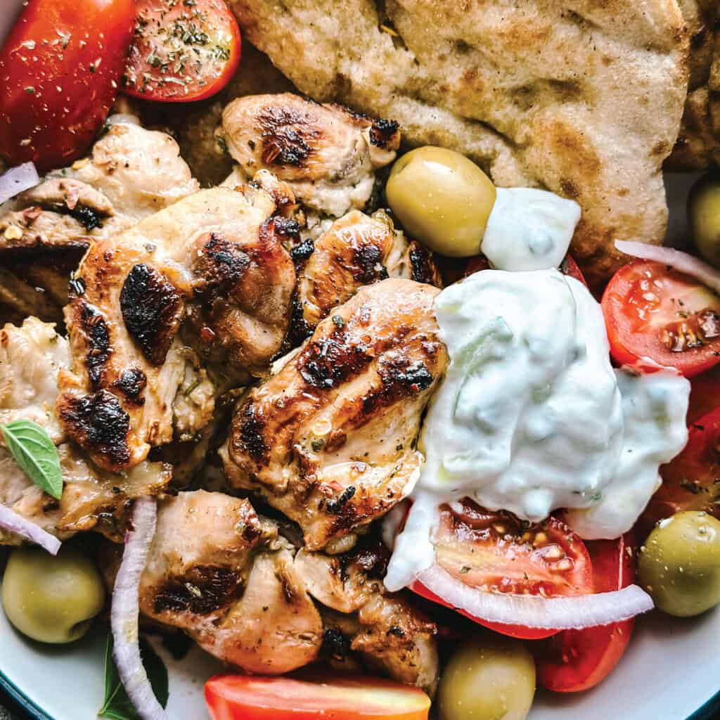 A tzatziki chicken bowl with tomatoes, tzatziki and pita on a table.