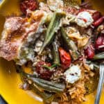 Baked rice with okra and feta, with a piece of bread on a plate with a fork, on a table with more bread and a cloth napkin.