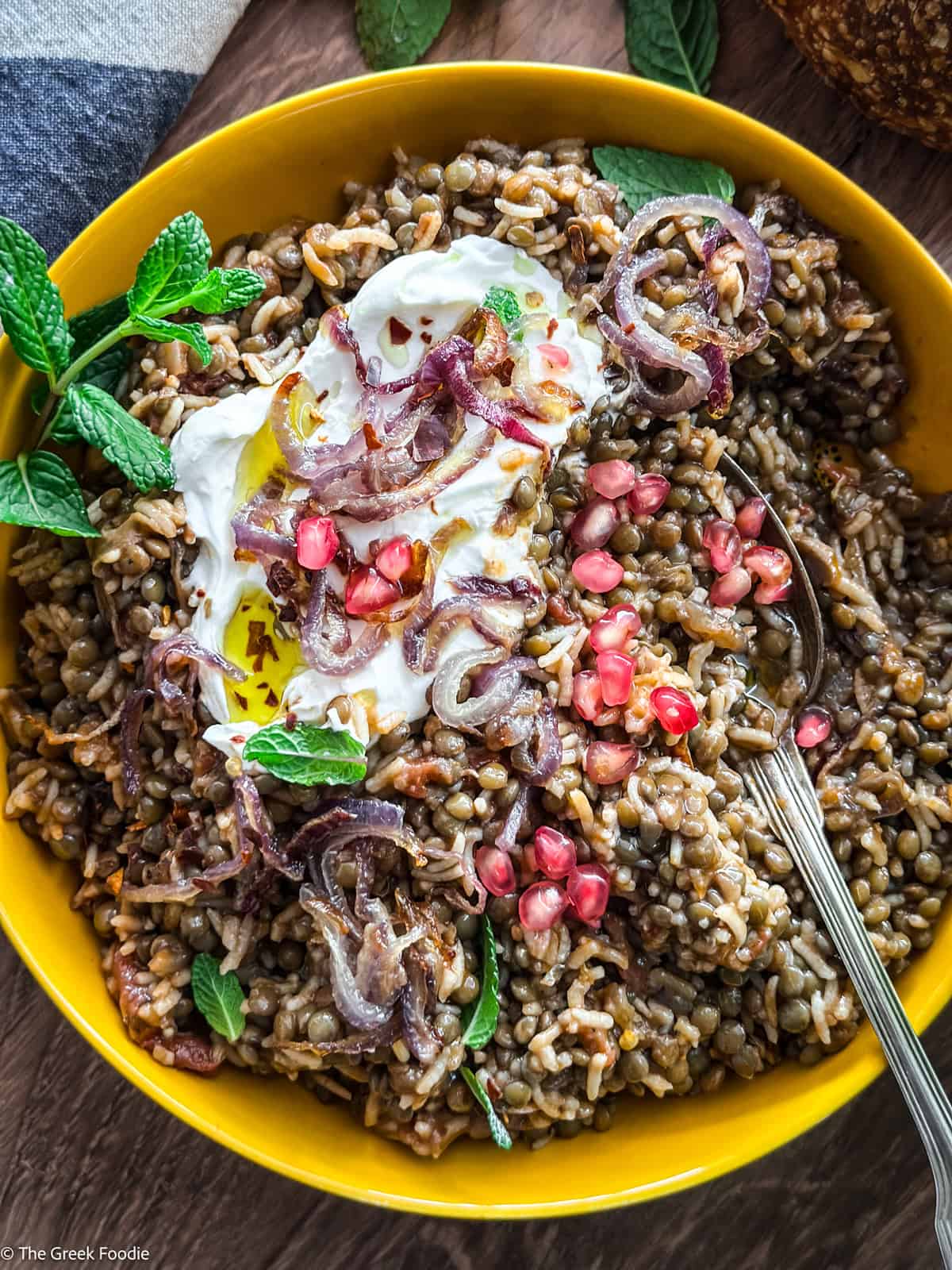 A yellow plate with fakorizo-lentils with rice, pomegranate seeds and spearmint, and a spoon.