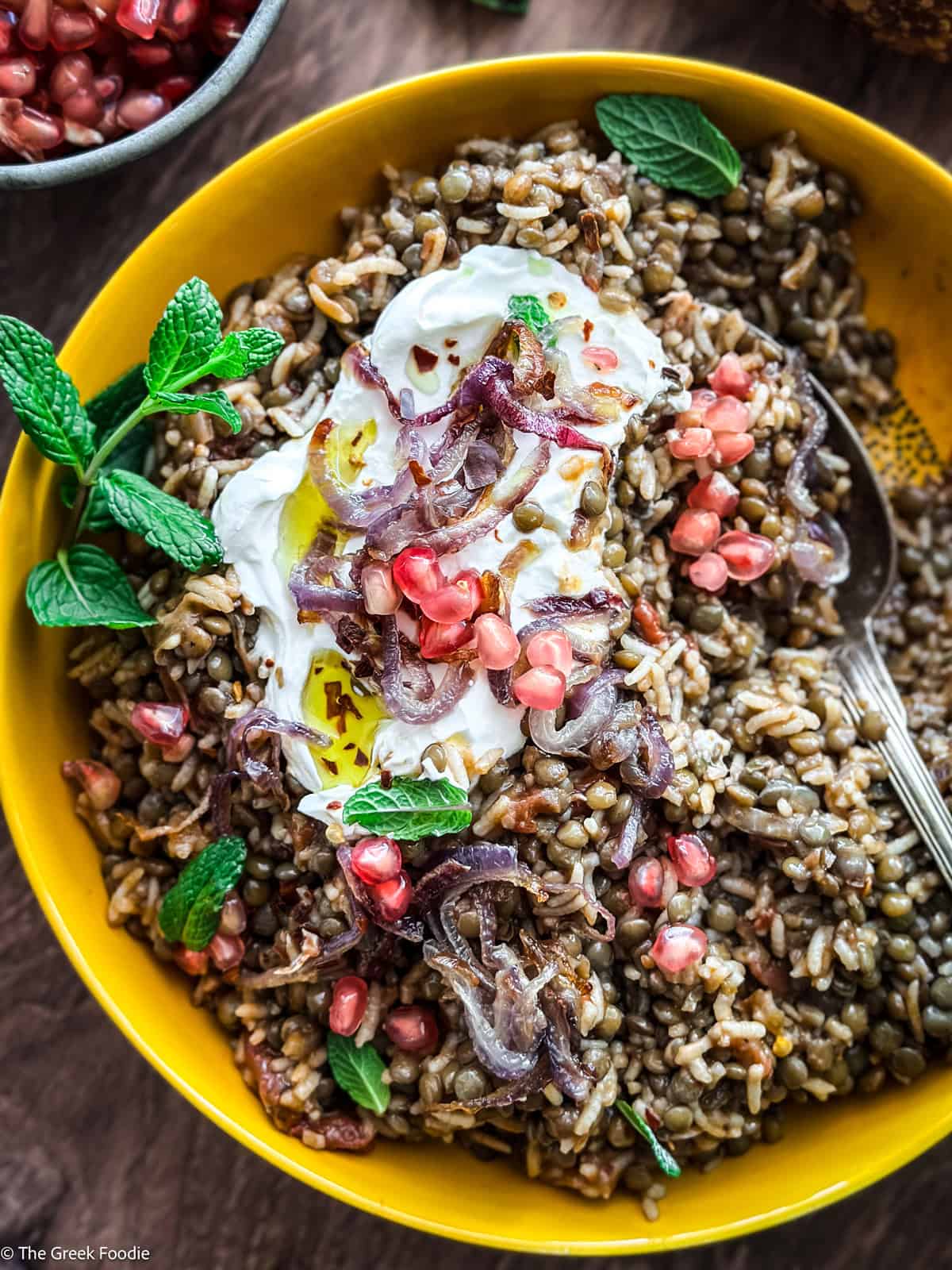 A yellow plate with fakorizo-lentils with rice, pomegranate seeds and spearmint, and a spoon.