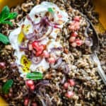 A yellow plate with fakorizo-lentils with rice, pomegranate seeds and spearmint, and a spoon.