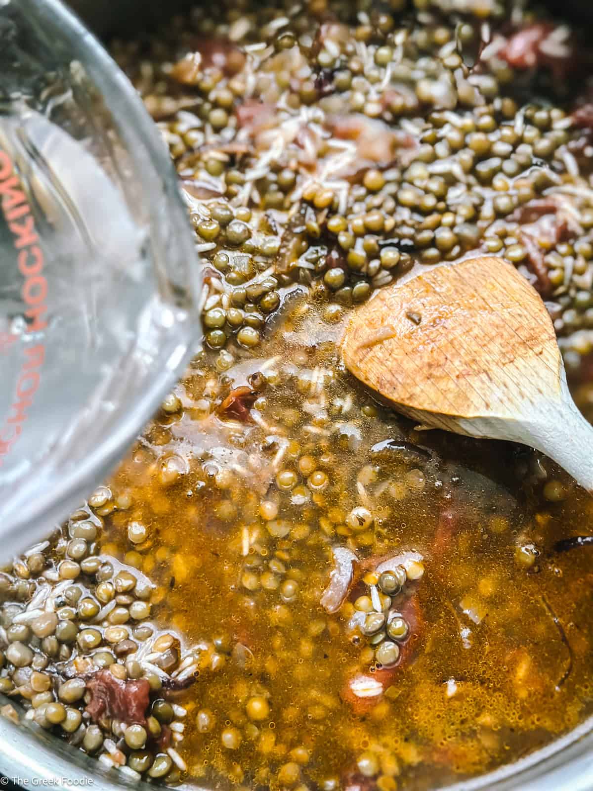 Water poured into lentils and rice with onions and a wooden spoon.