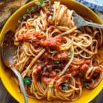 A plate with spaghetti and Greek tomato sauce, a fork and a spoon.