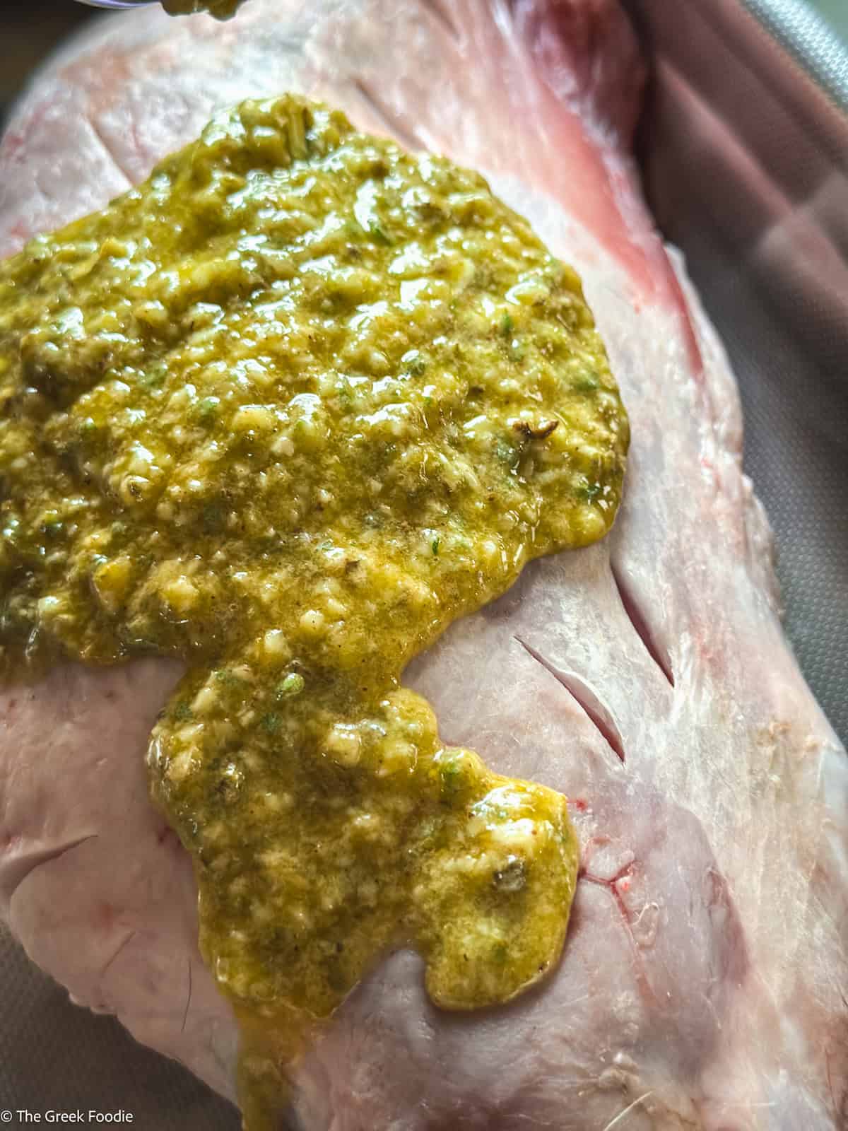 Garlic herb marinade on a piece of lamb in a roasting pan.
