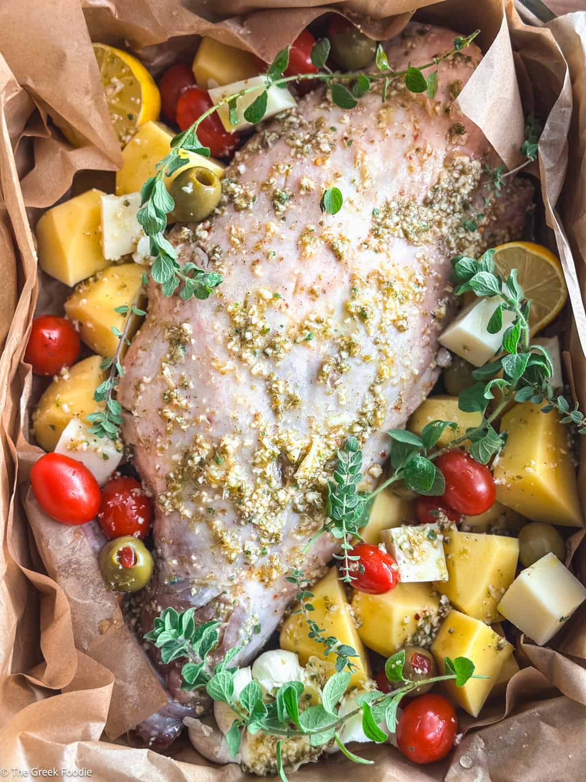 A leg of lamb kleftiko with tomatoes, potatoes, olives and herbs in parchment paper.