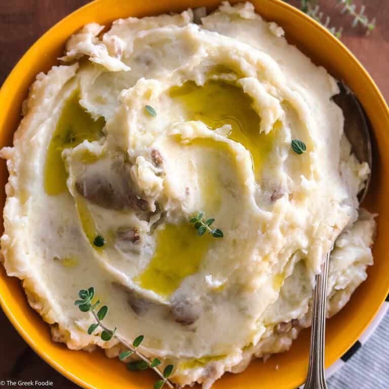 A yellow bowl with olive oil mashed potatoes, herbs and a spoon.