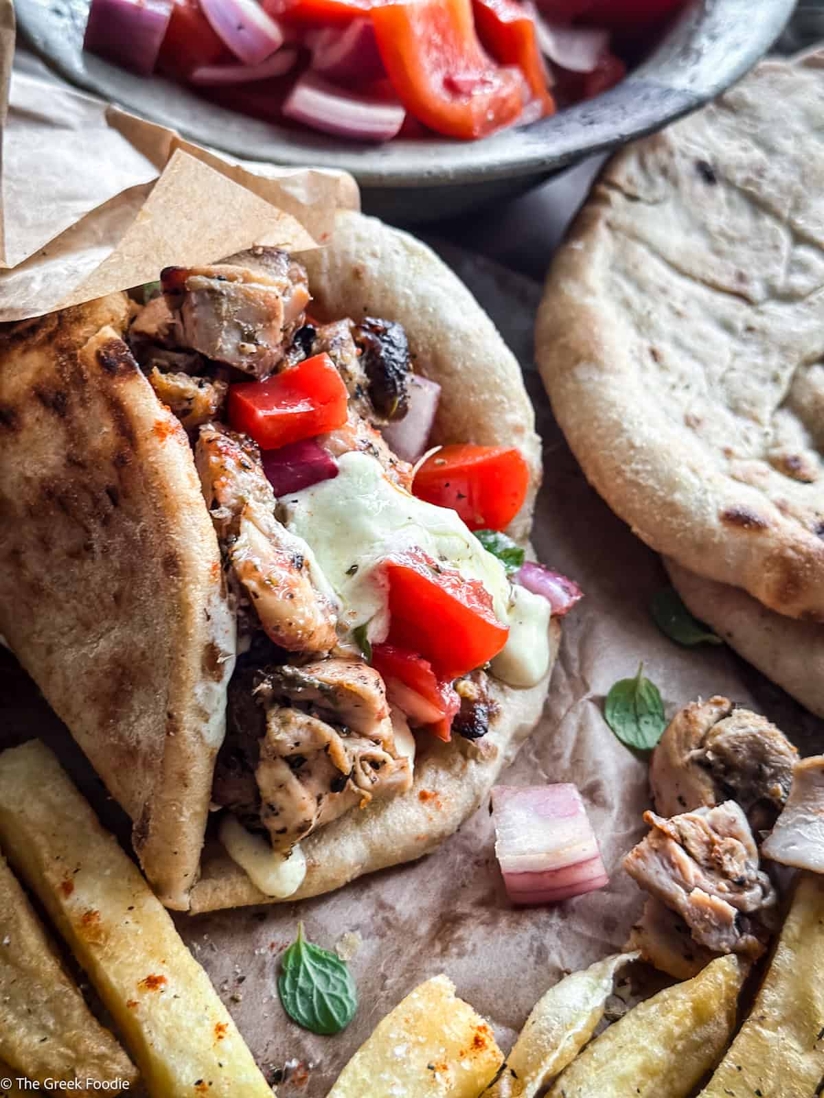 A chicken gyros souvlaki wrapped on paper, next to pita and fries.