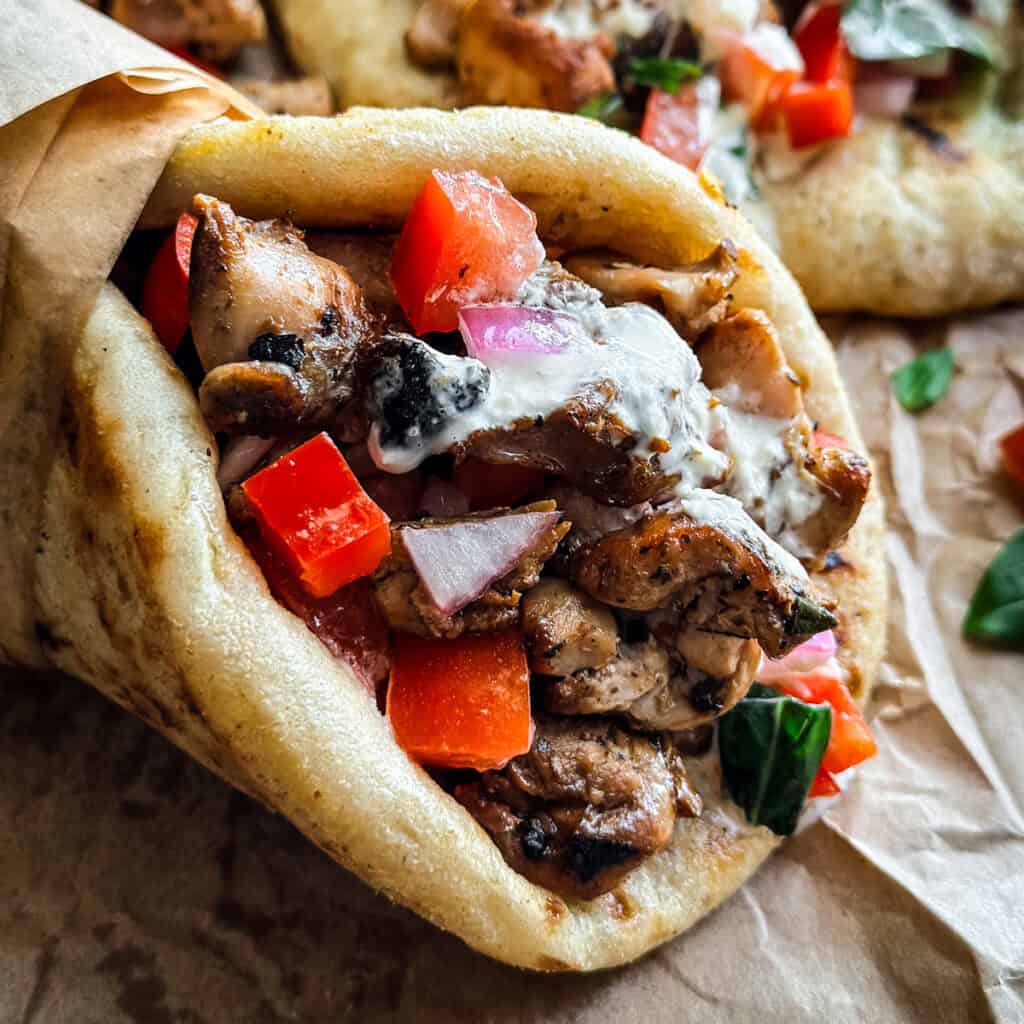A chicken gyros souvlaki wrapped on paper, next to pita and fries.