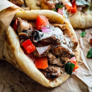 A chicken gyros souvlaki wrapped on paper, next to pita and fries.