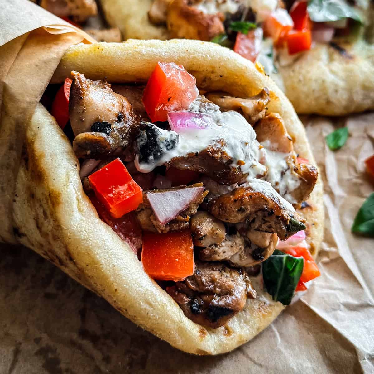 A chicken gyros souvlaki wrapped on paper, next to pita and fries.