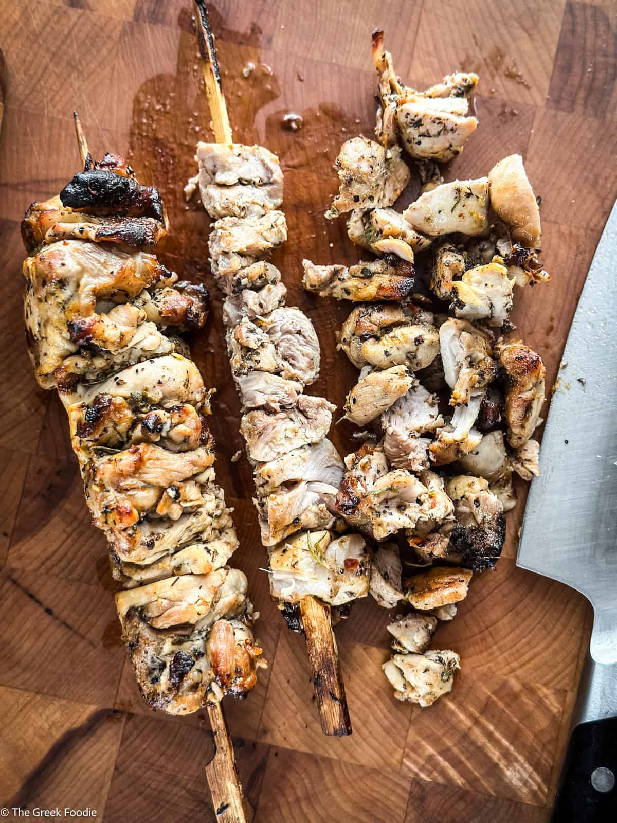 Chicken skewers on parchment paper some cut on the side, with a chefs knife.