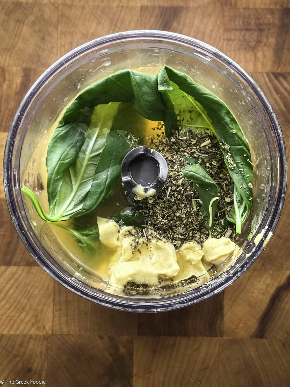 Basil, mustard, oregano and juice in a food processor on a wooden table.
