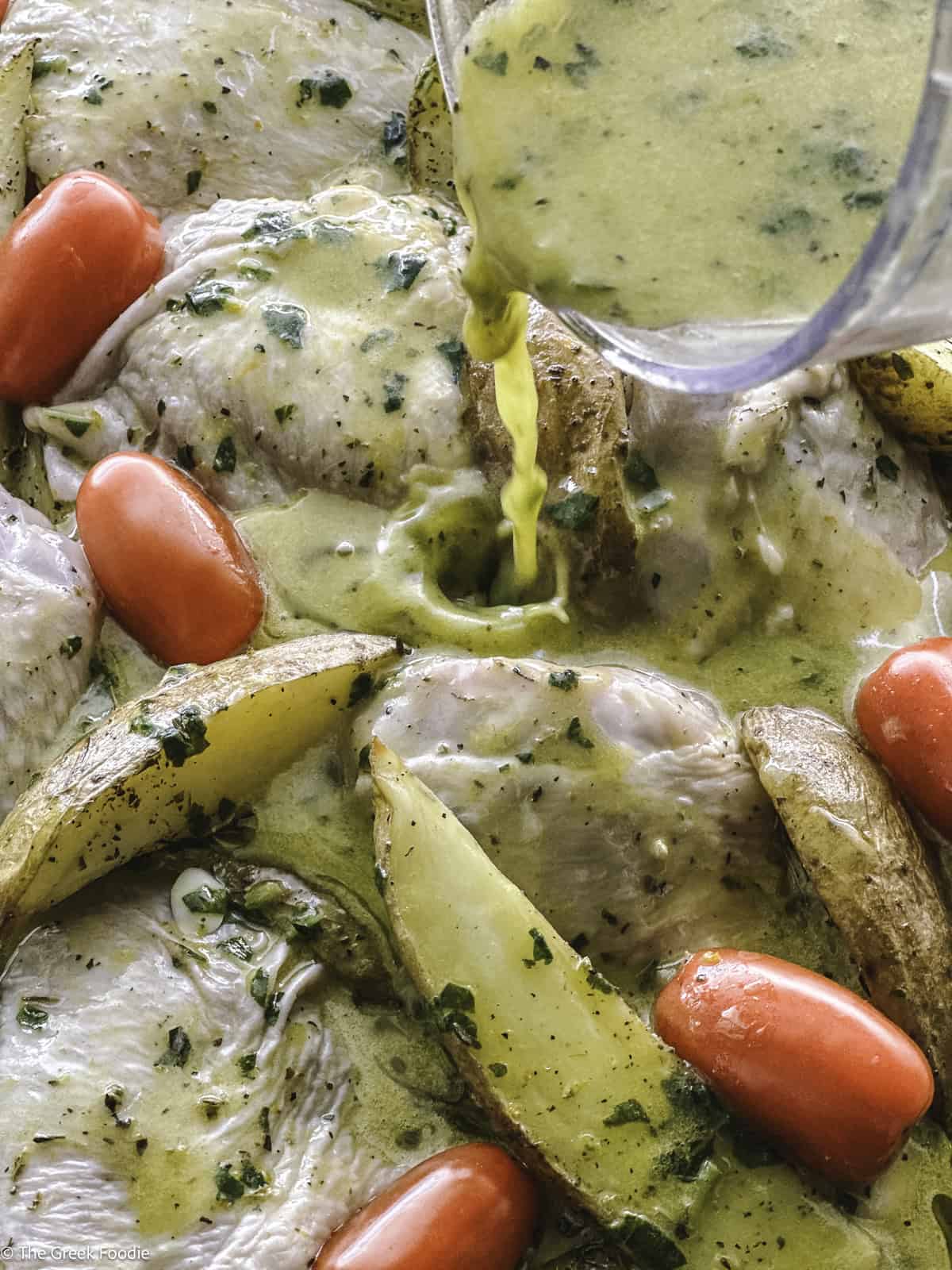 A bowl pouring marinade over chicken and potatoes.