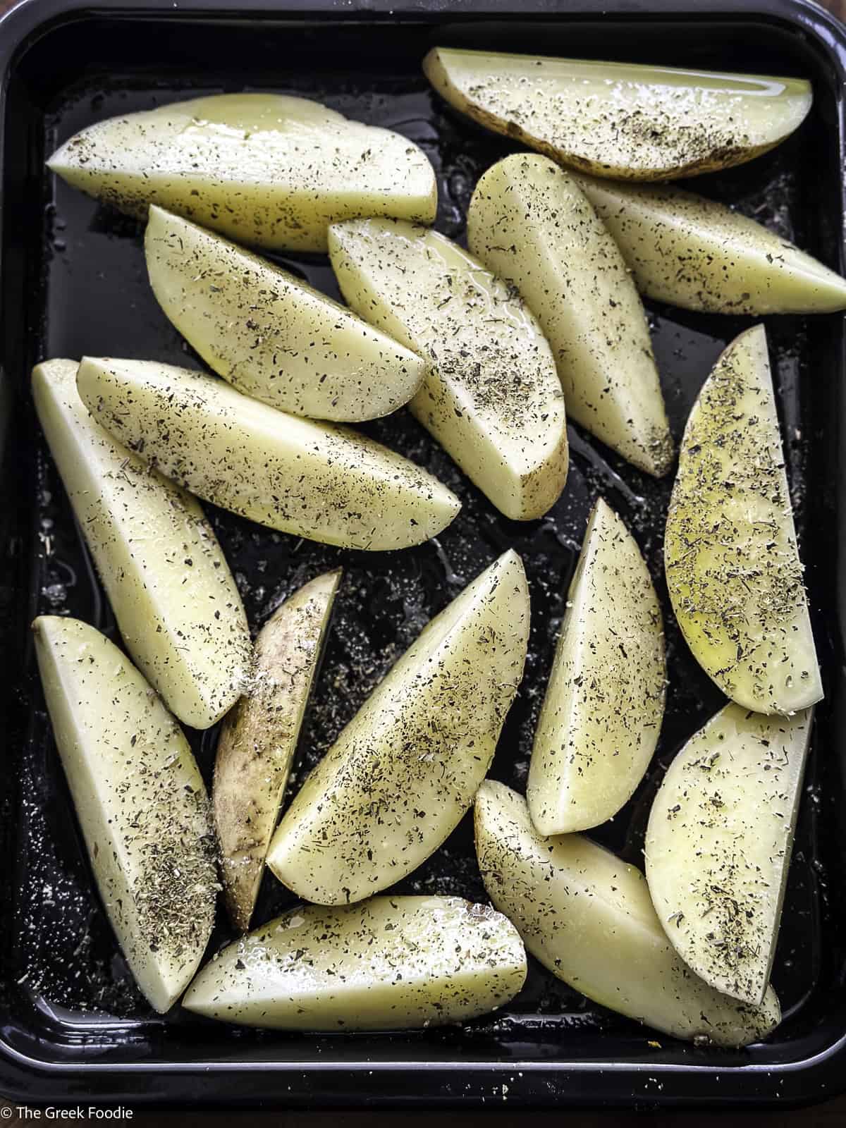 Potato wedges in a pan with seasonings.