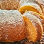 A Greek yogurt cake with a piece taken out on a bronze wire rack on a table.