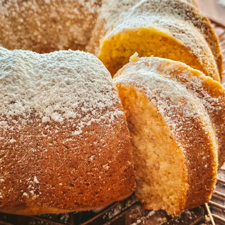 A Greek yogurt cake with a piece taken out on a bronze wire rack on a table.