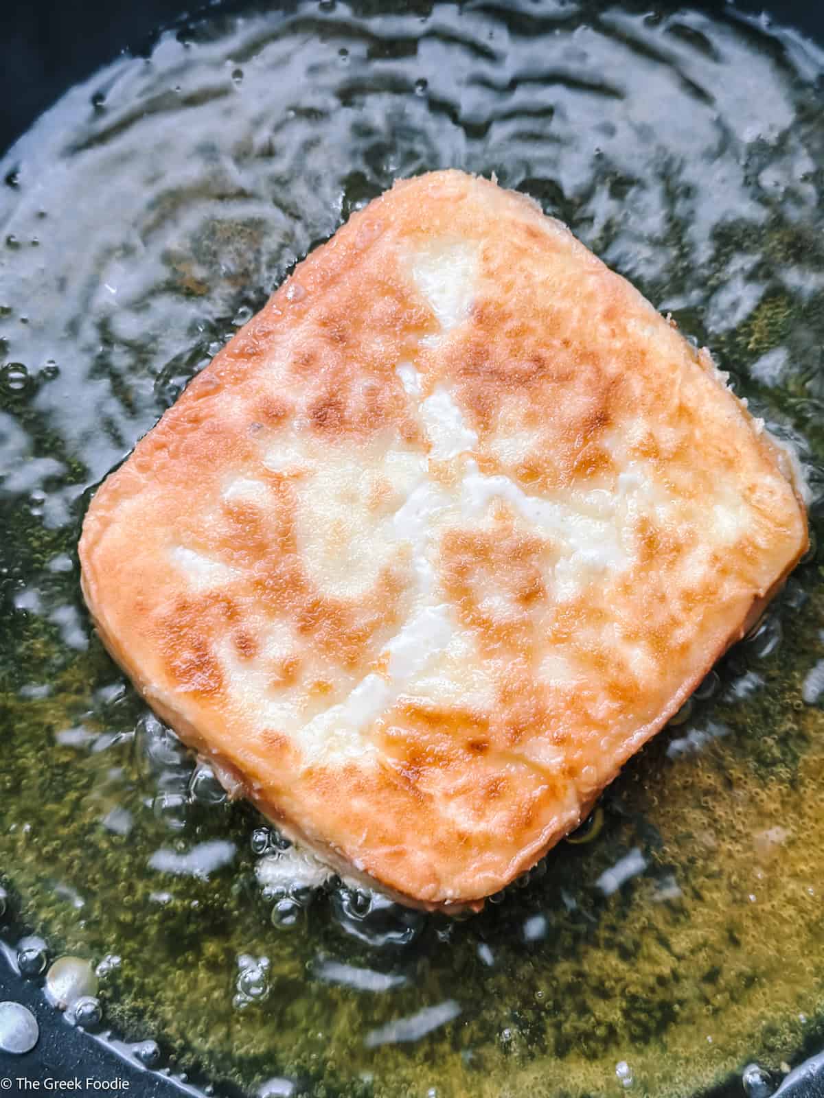 A piece of cheese frying in olive oil.