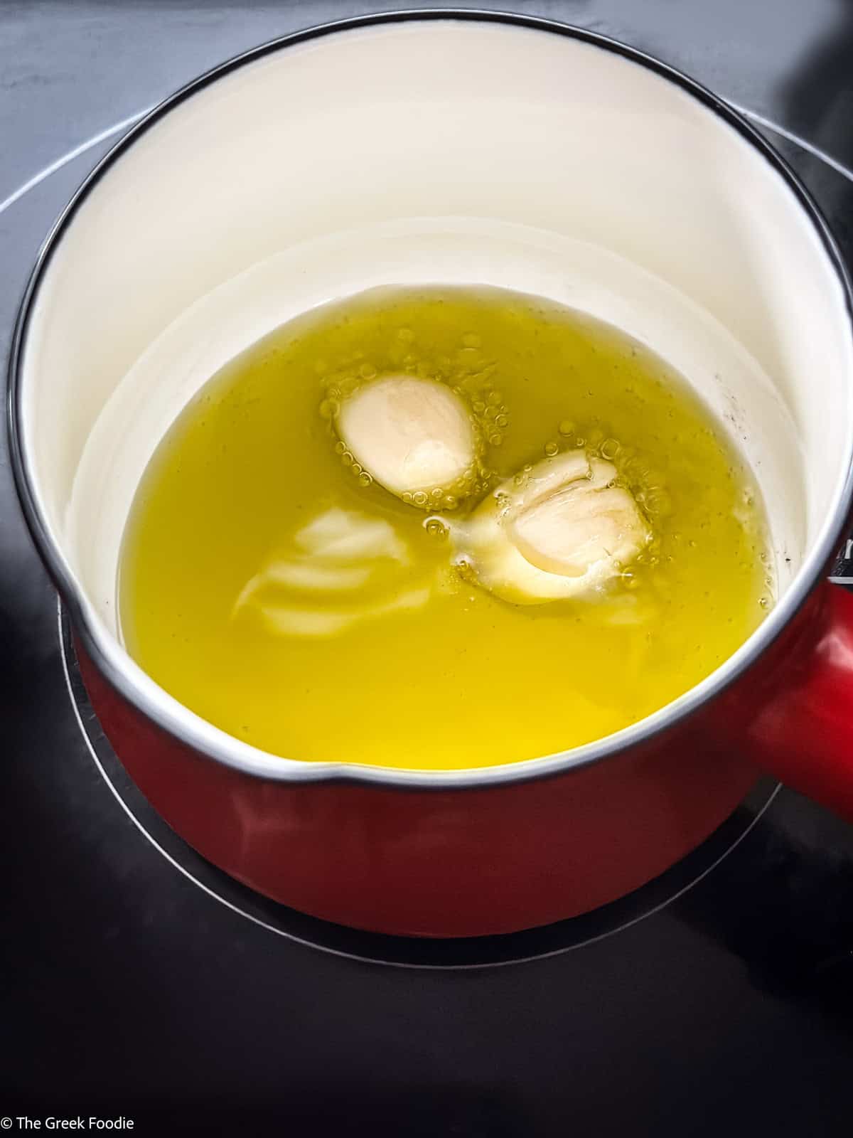 Two garlic cloves in olive oil in a saucepan.