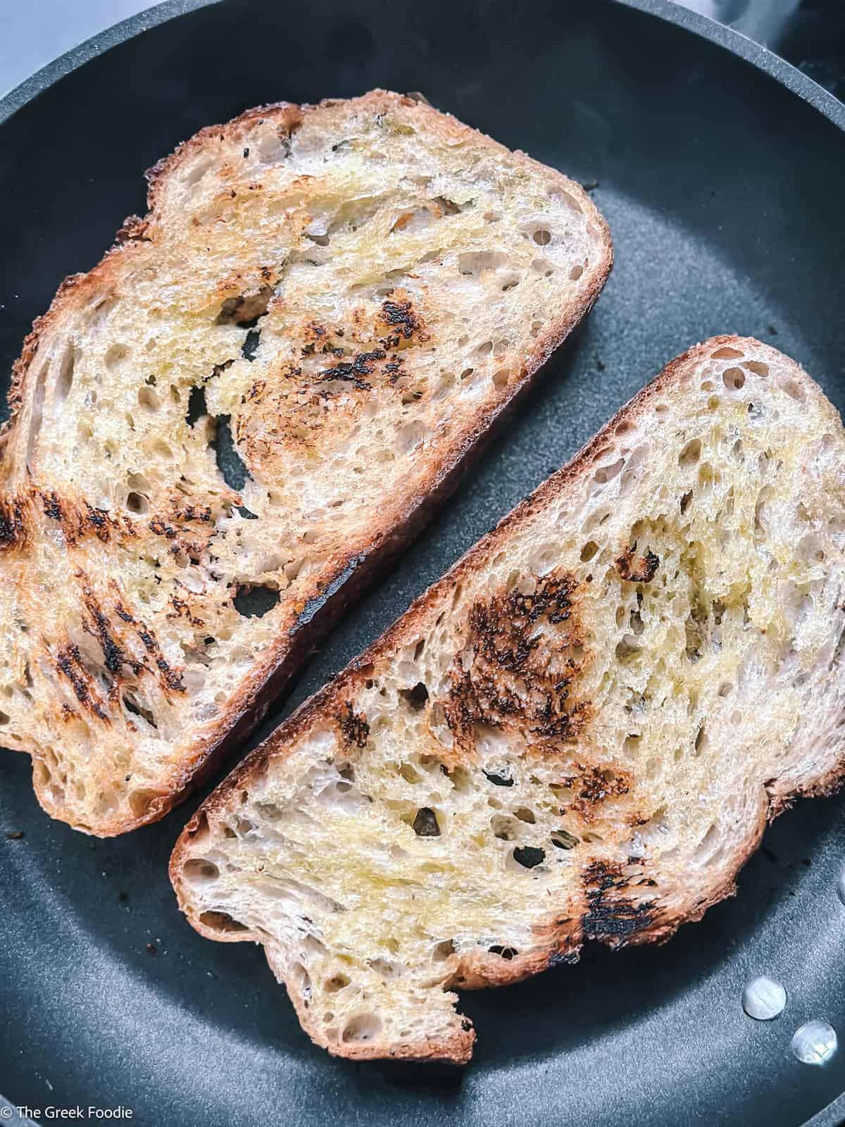 Two bread slices toasting on a pan.