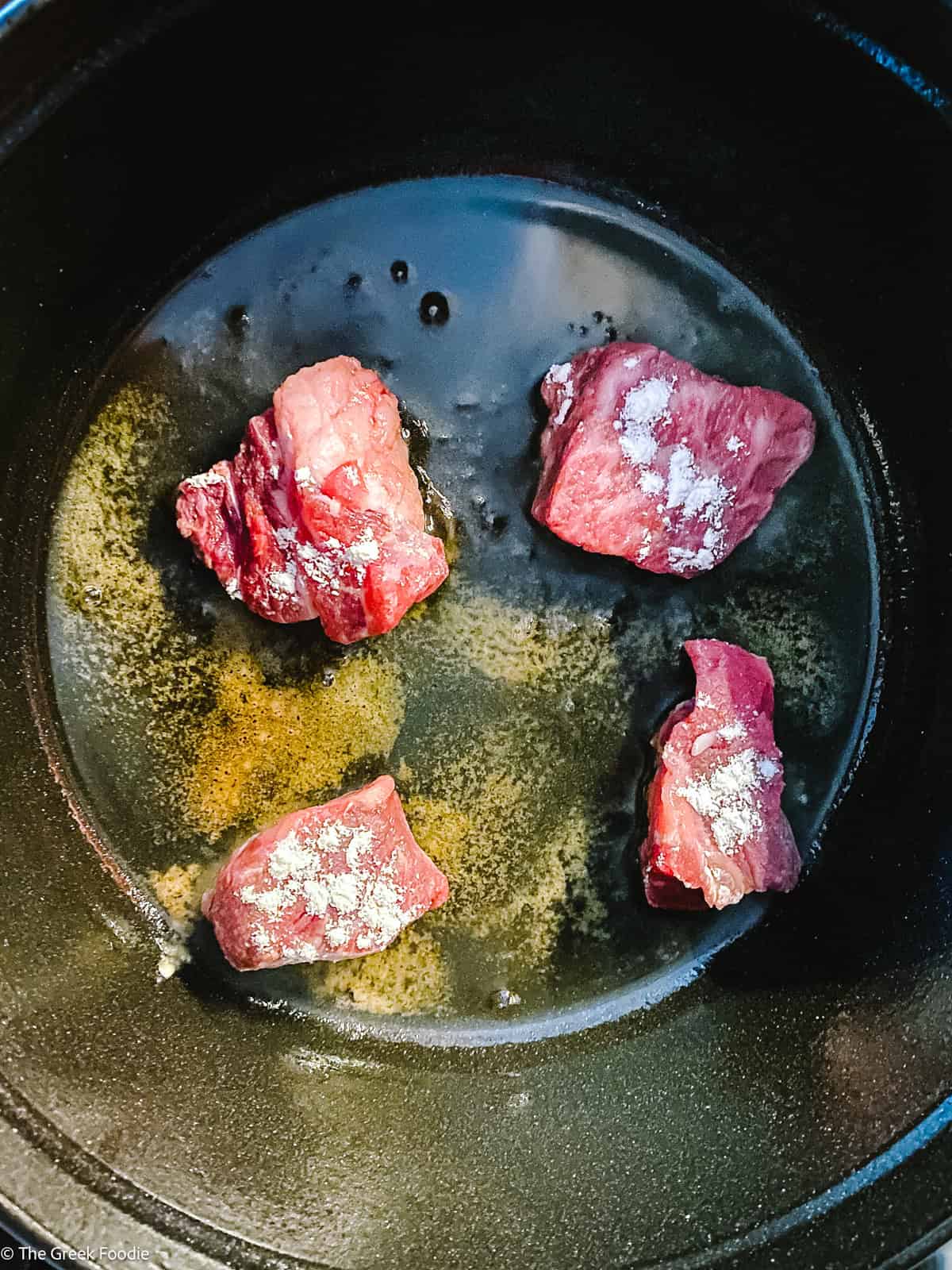 Four pieces of beef searing in a pot.