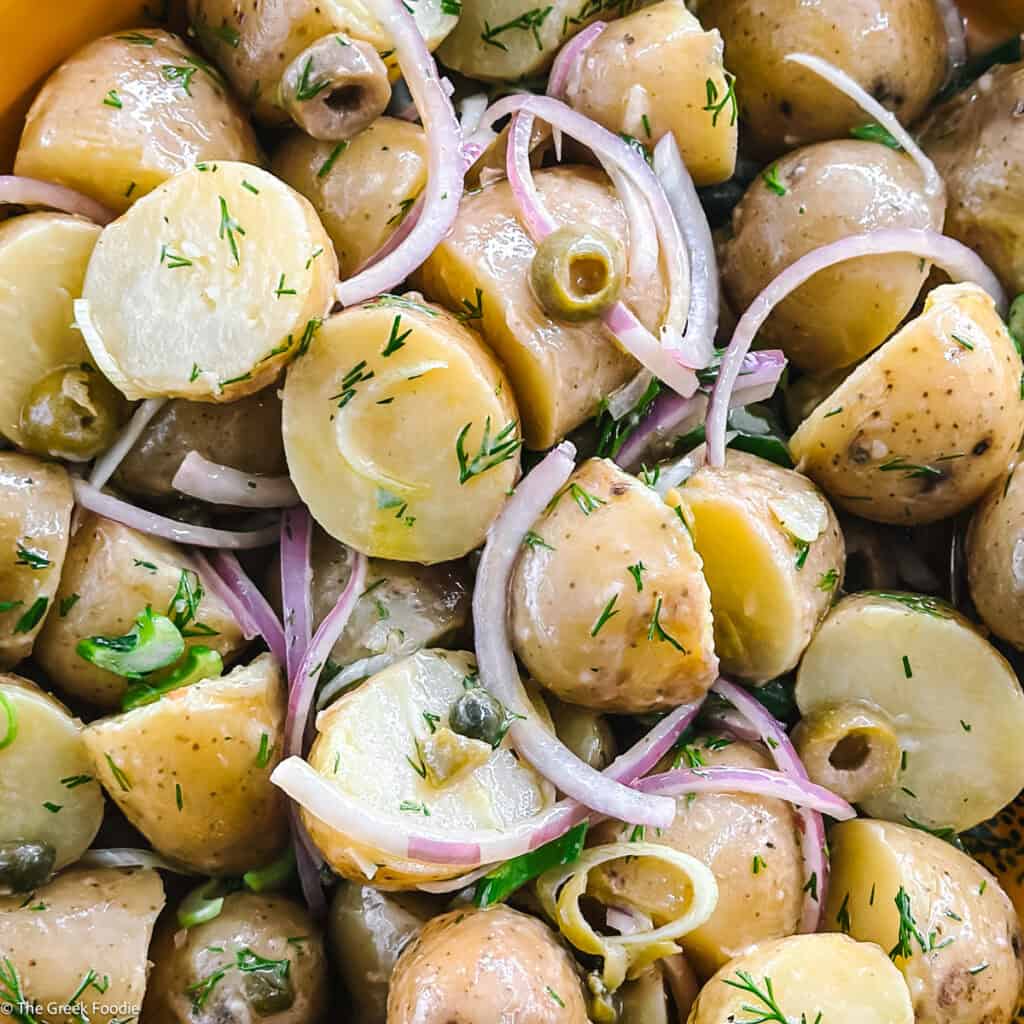 Greek potato salad with olives, capers, dill and red onion in a yellow bowl