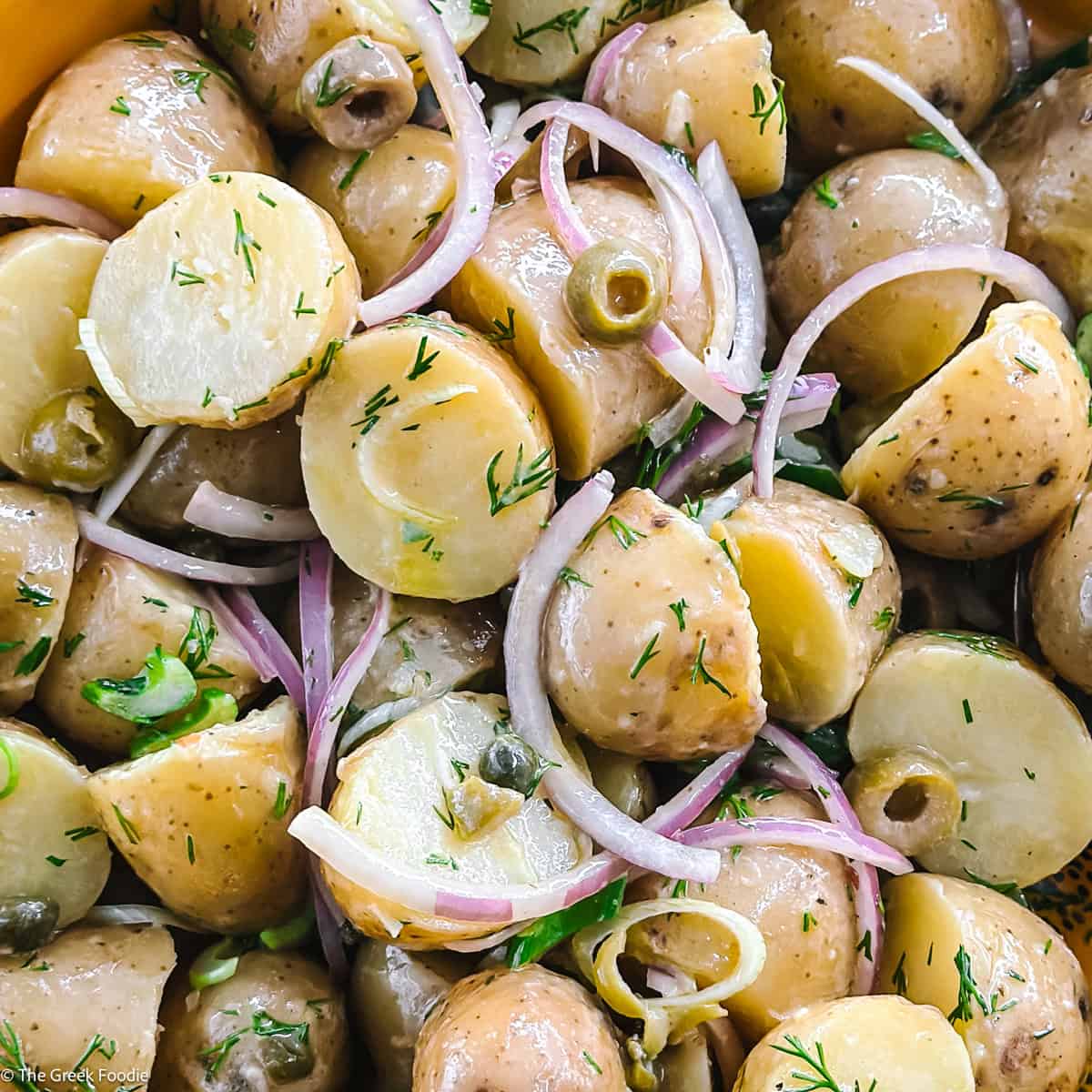 Greek potato salad with olives, capers, dill and red onion in a yellow bowl