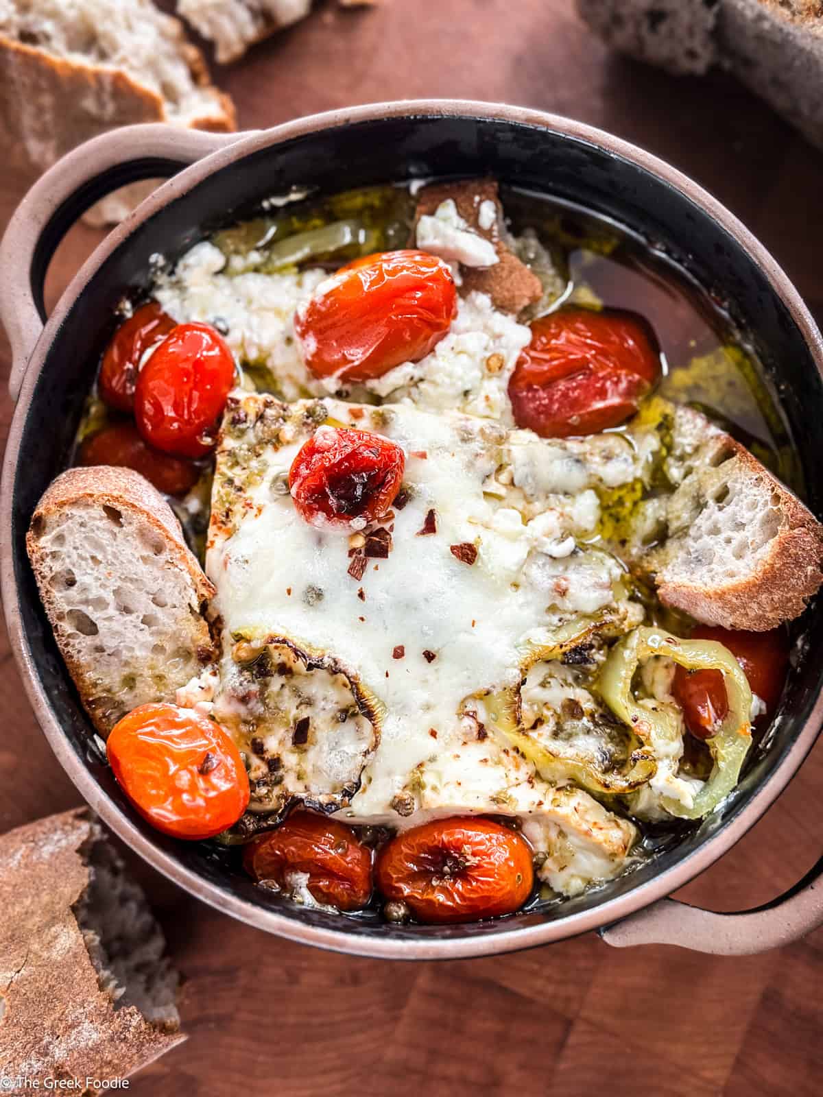 A ceramic dish with baked feta dip-bouyourdi with pieces of bread on a table.