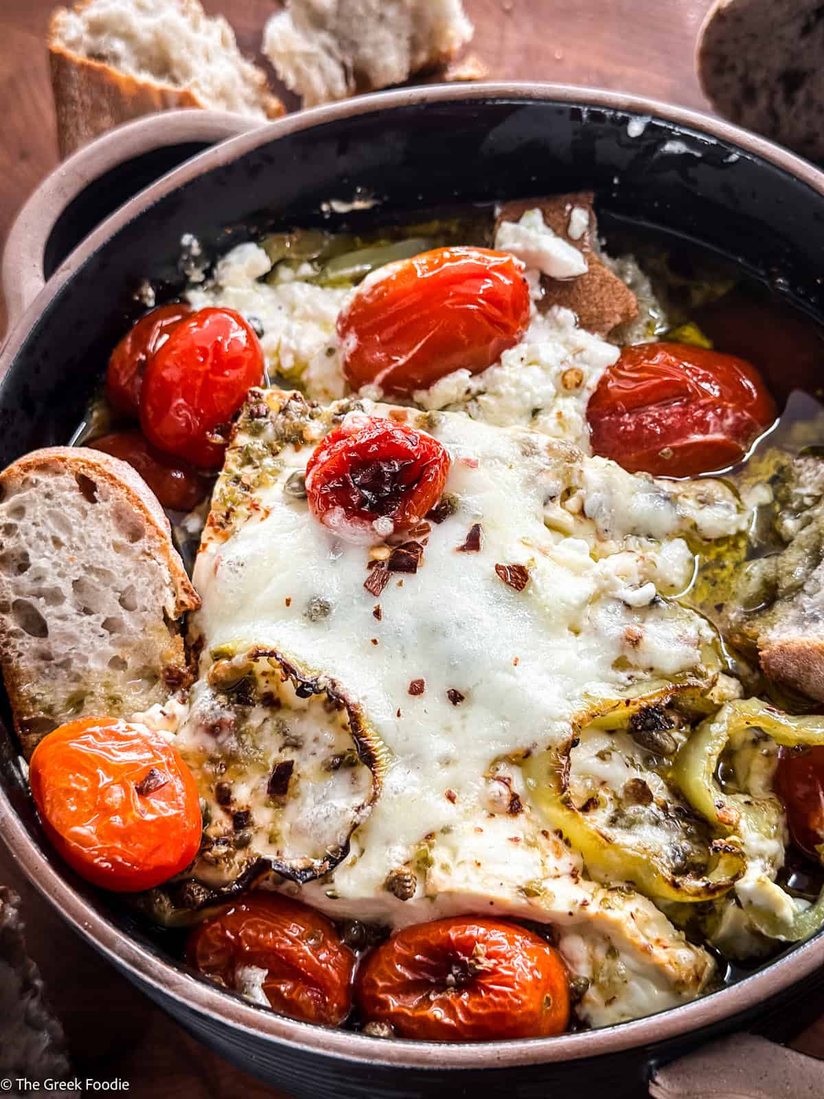 A ceramic dish with baked feta dip-bouyourdi with pieces of bread on a table.