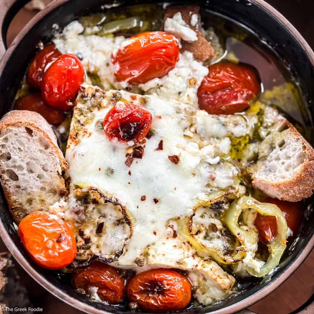 A ceramic dish with baked feta dip-bouyourdi with pieces of bread on a table.