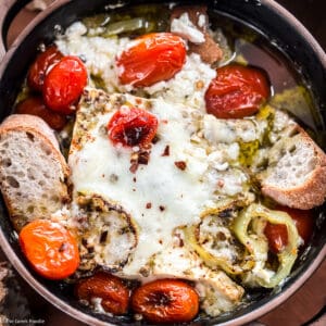 A ceramic dish with baked feta dip-bouyourdi with pieces of bread on a table.